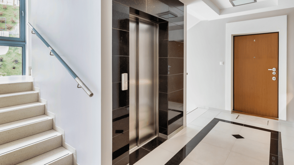 A modern apartment building interior featuring a stainless steel elevator, a staircase with a glass railing, and a secure entry door. This highlights the importance of seamless access control in multifamily properties, showcasing how RemoteLock enables centralized management of common areas and resident access.